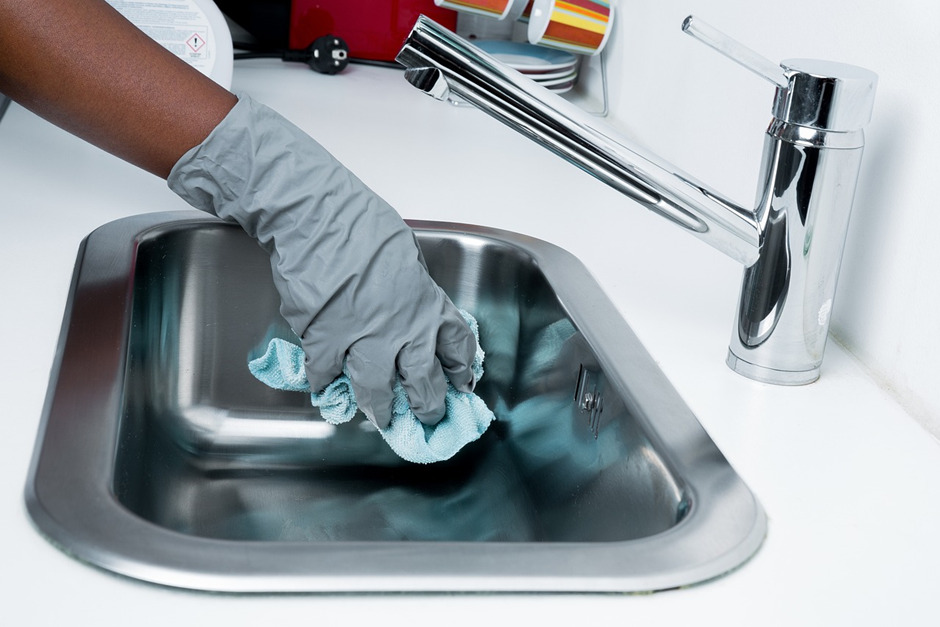 A person wearing gloves is wiping the sink