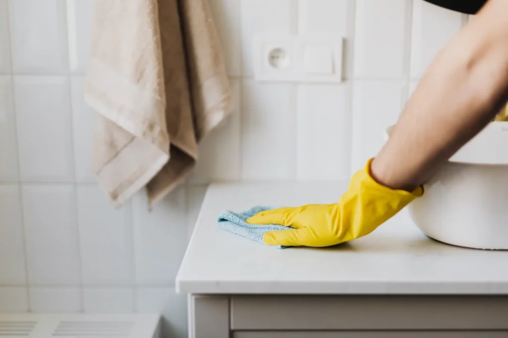 house cleaner wearing a yellow glove cleaning a bathroom countertop with a rag at one of the top house cleaning companies in west chester pa.